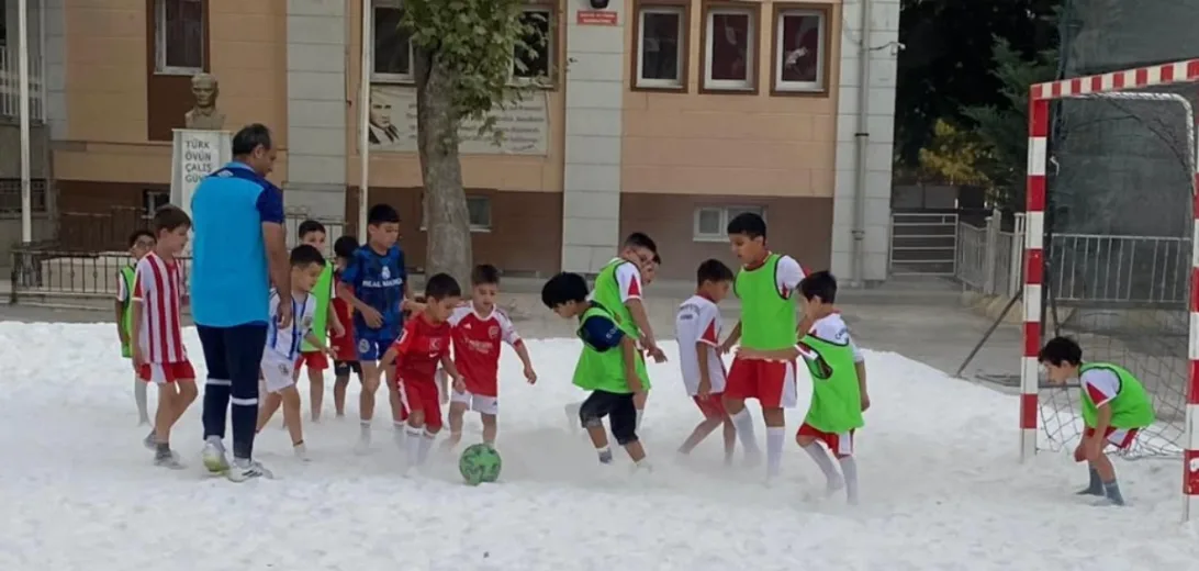 Karla kaplı sahada top oynayan öğrenciler
